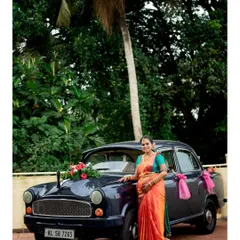 A full length portrait showcasing the expecting mother beside the decorated vintage car. This shot highlights the entire look, from the vibrant saree to the beautiful natural backdrop of Udupi.