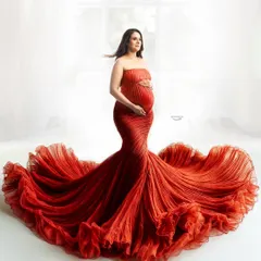 A classic and powerful pose in a strapless red mermaid gown. The ruffled train spreads out beautifully, creating a strong silhouette against the bright, high-key background for a glamorous maternity photo.