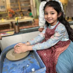 This young artist is ready to create her masterpiece. I provide aprons and a supportive environment so kids can dive into the fun of pottery without any worries.