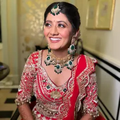 A joyful bride with a natural and radiant makeup look. The soft eyeshadow and glowing skin perfectly complement her traditional red lehenga and emerald jewellery.