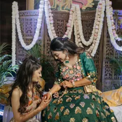 The decor should be the perfect backdrop for candid moments like this one. The traditional wooden screen and fresh flower garlands create a rich, textured background that enhances the beauty of the Mehendi ceremony.