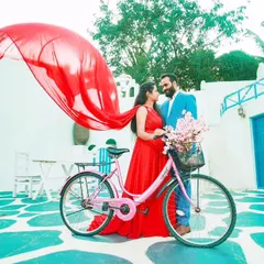 A playful and vibrant pre-wedding shoot in a Santorini-themed setting. The client's red flying gown adds a pop of color, perfectly complementing the fun, summery vibe.