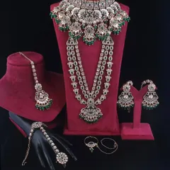 A complete reverse AD bridal set with green stones, displayed to show all the matching pieces: choker, rani haar, earrings, maang tikka, and hathphool.