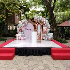 The full stage setup for the naming ceremony, showing the backdrop and balloon decor on a raised platform with a floral-printed floor. This outdoor setup is perfect for a daytime event.