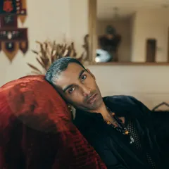 A close-up, moody portrait of artist Nilikkhimani at his home, using the rich texture of a red velvet couch to add depth.