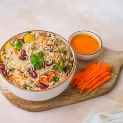 A light and healthy vegetable rice bowl with kidney beans, served on a wooden platter against a bright background.