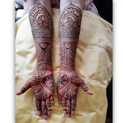 A heavy and intricate Indian design for the bride's mom, filled with floral patterns and peacock motifs extending up the arms.