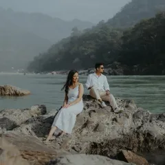 A serene pre-wedding portrait in Rishikesh, with the couple sitting on the rocks by the river, surrounded by misty mountains. This showcases my love for destination couple shoots.