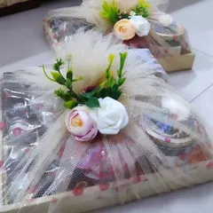 A gourmet treats basket in a wooden tray, elegantly wrapped in net with floral decorations.