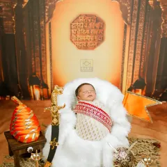 A newborn photoshoot with a 'Bal Shivaji' theme. The setup includes a miniature sword, a saffron flag, and the Rajmudra, creating a powerful and unique portrait.