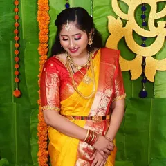 A beautiful, happy client ready for her daughter's naming ceremony. The makeup is bright and festive, with a pop of color on the eyes and lips to match her vibrant yellow and red saree.