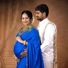 A beautiful portrait of an expecting couple in traditional attire. The vibrant blue saree, adorned with a peacock feather, adds a touch of divine symbolism to the image.