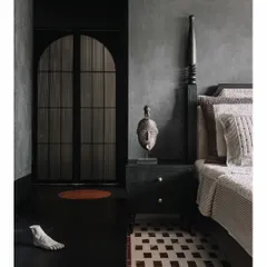 Another view of the 'Aria' master bedroom, showing the interplay of textures and forms. The dark, moody IPS walls and black wood furniture are balanced by the geometric pattern of the floor and unique artifacts, like the sculpted foot and African mask, that add a personal narrative.