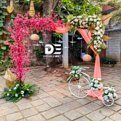 A whimsical and colorful entrance piece for an outdoor event. I combined a vibrant pink bougainvillea arch with a decorative white bicycle filled with flowers, creating a perfect photo spot and a cheerful welcome.