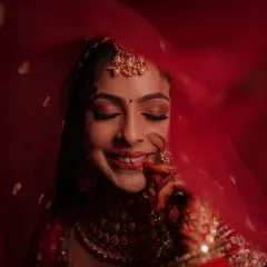 The quintessential blushing bride. This look focuses on a flawless, glowing base, soft smokey eyes, and a classic red lip, all framed by a delicate red veil for a timeless wedding day portrait.
