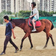 Your safety and confidence are our top priorities. This image shows a beginner rider on her first lesson, with one of our experienced trainers leading the horse to ensure a comfortable and secure introduction to riding.