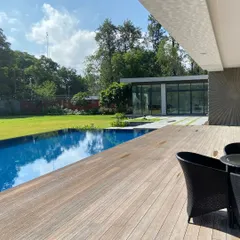 A view from the veranda across the wooden pool deck to the expansive lawn of a New Delhi farmhouse. We design outdoor spaces that serve as extensions of the home, perfect for both quiet afternoons and grand entertaining.