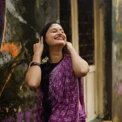 The pure bliss of a rainy day. This candid shot captures a moment of uninhibited laughter, with the model in a lovely purple bandhani-print saree against a rustic, graffiti-covered wall.