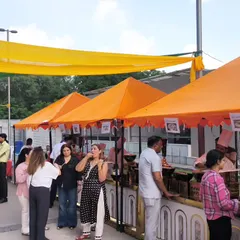 Guests enjoying our food at a vibrant outdoor event. We set up multiple stalls with colorful canopies, creating a festive, market-like atmosphere for everyone to explore different cuisines.