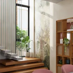 A minimalist floating staircase with wooden treads and vertical steel cables for a railing. A large window and a tropical mural wall bring light and nature into the space.