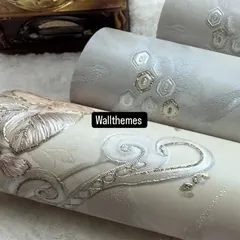 Close-up of textured wallpaper rolls in neutral tones with elegant silver and gold embroidered-look details.