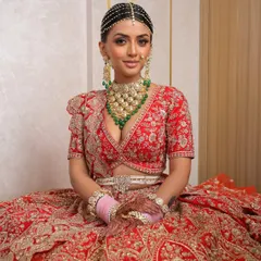 A seated portrait capturing the grandeur and grace of the bride. The rich red lehenga and intricate jewelry are balanced with makeup that is both glamorous and refined, perfect for the main event.