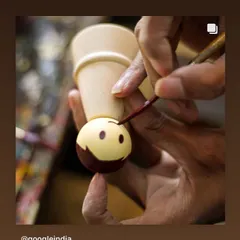 A close-up of an artisan's steady hand painting a cheerful face onto a wooden doll. This delicate work requires immense precision and is what gives our toys their distinct character and charm.