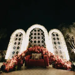 A beautiful photo-op area with a red sofa set against white latticework arches and lush red florals. A perfect spot for guests to capture memories.