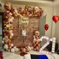 A glamorous 21st birthday setup designed for stunning photos. This decoration features a dazzling rose gold sequin wall, a custom neon sign, and an organic balloon arch in rose gold and white, complemented by large '21' marquee lights.