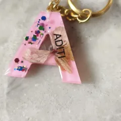 A personalized keychain with the initial 'A' for Aditi. This piece was made with pink resin, glitter, and delicate dried flowers, making it a perfect custom gift.