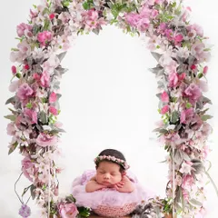 This sleeping newborn is framed by a beautiful arch of pink flowers while resting on a swing, creating a breathtaking and whimsical floral portrait.