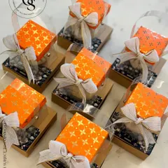 Cute return favors for Ganesh Chaturthi. These small, bright orange boxes are filled with treats and presented in a clear carrier with a simple ribbon, making them a perfect token of thanks for guests.