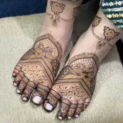 This foot mehandi features graceful peacock motifs with detailed check patterns. The design extends to a delicate vine on the ankle, resembling a beautiful piece of jewelry.