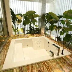 A luxurious jacuzzi tub set in a bed of green and gold onyx-style marble, surrounded by lush indoor plants. This design blurs the line between a bathroom and a tropical spa retreat.