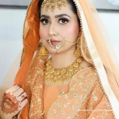 A beautiful Sikh bride in a peach-colored suit. The makeup is soft and radiant, with a focus on her eyes, and the look is completed with a traditional nath and maang tikka.