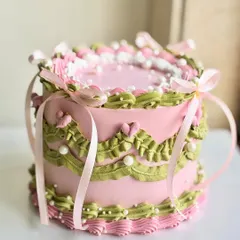 A dreamy vintage cake in pink and green, adorned with intricate piping, edible pearls, and delicate pink ribbons tied into bows for a fairytale finish.