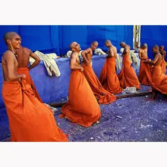 A candid moment of joy and camaraderie among young Buddhist monks. The vibrant orange of their robes against the stark blue wall creates a powerful color contrast, highlighting a moment of uninhibited laughter.