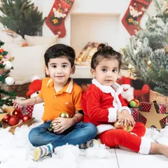 Two siblings sitting in a festive Christmas setup. This photo captures the wonder and excitement of the holiday season for young children.