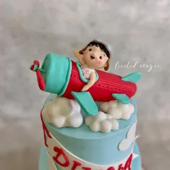 Look at this little pilot waving from her aeroplane! This handmade fondant topper was created for a second birthday, showing that even the smallest details, like the cute expression, are crafted with love to make the cake special.