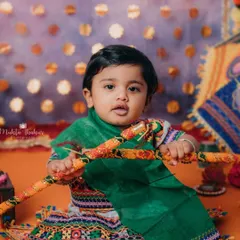 This little Radha is ready to steal the show with her dandiya sticks. The vibrant colors of the Navratri setup make for such joyful photos.