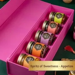 The 'Spritz of Sweetness' box is a delightful gift for a wedding or engagement. It features a row of five jars filled with assorted mouth fresheners and sweet treats in a vibrant pink box.