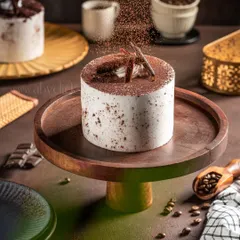 A tiramisu-inspired cake on a wooden stand, with cocoa powder being dusted on top to capture a moment of action and add a sense of freshness.