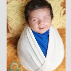That fleeting, sleepy smile is what we live to capture. This little one, wrapped snugly in white and blue, shows the pure joy of a newborn's dreams.