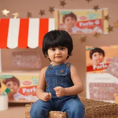 A close-up portrait for a nostalgic Parle-G themed first birthday shoot, with the baby girl in denim overalls looking just like the iconic biscuit brand's mascot.