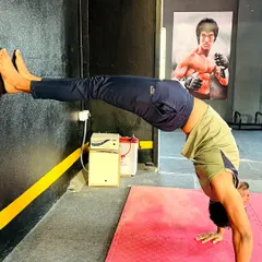 This wall-assisted handstand drill helps build endurance and proper alignment. Notice the Bruce Lee poster in the back for inspiration.
