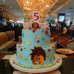 This two-tier Roblox cake is ready for a 5th birthday party. The bright blue cake is decorated with colorful blocks, stars, and a popular character from the game, making it a hit with young gamers.