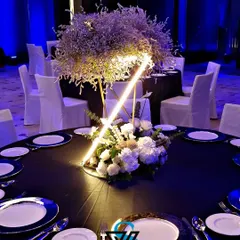 A dining table setup with a striking black tablecloth and blue-rimmed plates. The centerpiece combines natural elements with a modern, illuminated geometric structure, perfectly capturing the event's theme.
