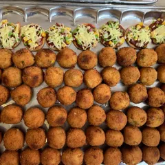 A tray of golden-brown Corn and Cheese Balls lined up next to Mini Veggie Pizzas, ready to be served at a party.