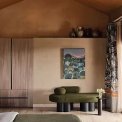 A view of a bedroom with a vaulted wooden ceiling and lime-washed walls. We used a sculptural olive green chaise and contemporary art to add character, balancing minimalism with curated, soulful pieces.