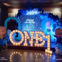 For a dramatic Boss Baby theme, I used a shimmering sequin backdrop and large light-up 'ONE' marquee letters. The blue and black balloon arrangement and character cutouts complete this nighttime party look.